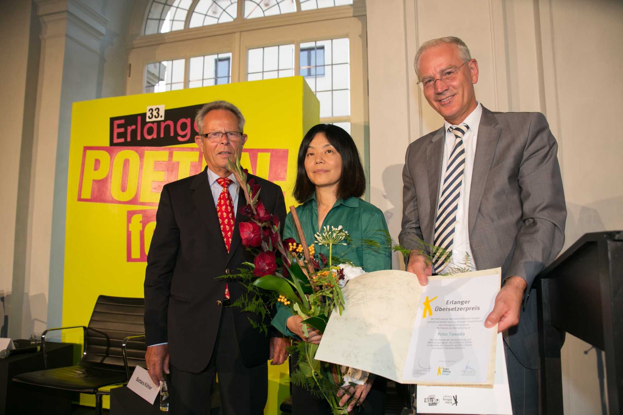 Gerd Wangemann, Yoko Tawada mit Blumenstrauß und OB Siegfried Balleis mit Unrkunde
