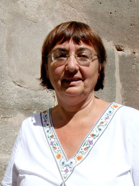 Frau mit Brille mit weißer Bluse vor Sandsteinmauer