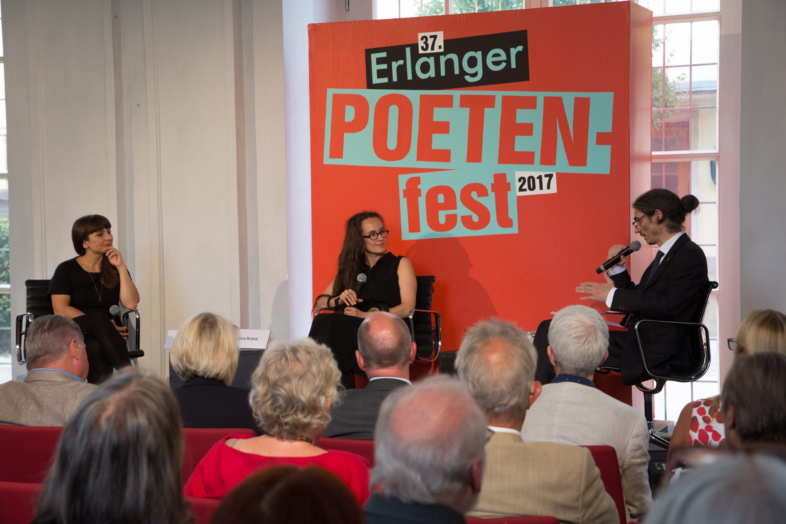 Dagmara Kraus auf dem Podium vor einer orangenen Leinwand welche mit 'Erlanger Poetenfest 2017' beschriftet ist
