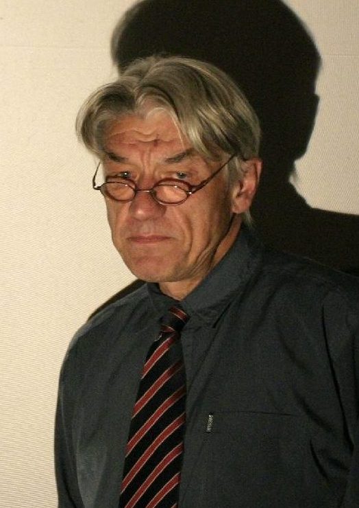 älterer Mann mit Brille, Krawatte und Hemd beim Vortrag am Projektor.