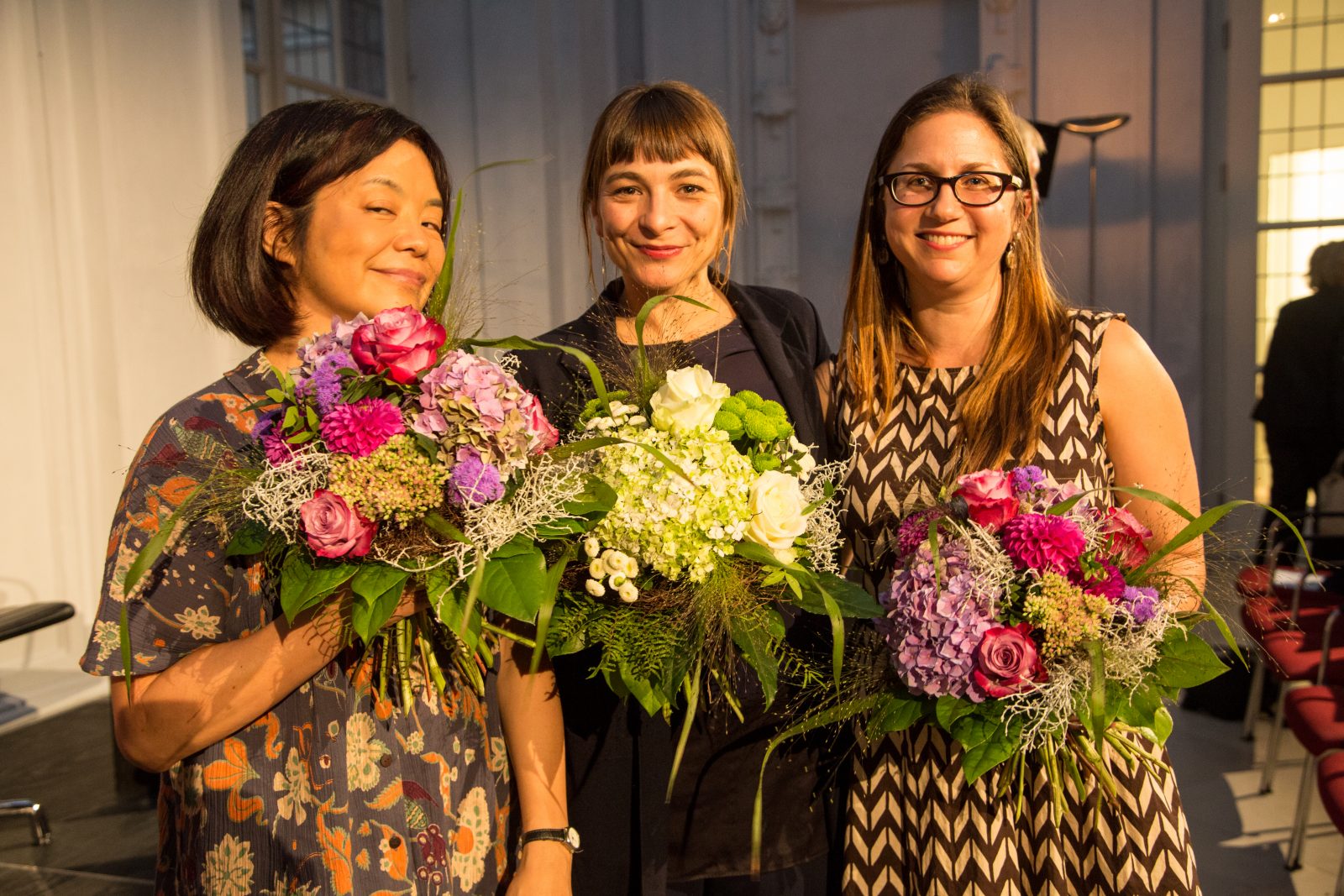 Drei Frauen mit Blumenstrauß und Kleidern lachen in die Kamera